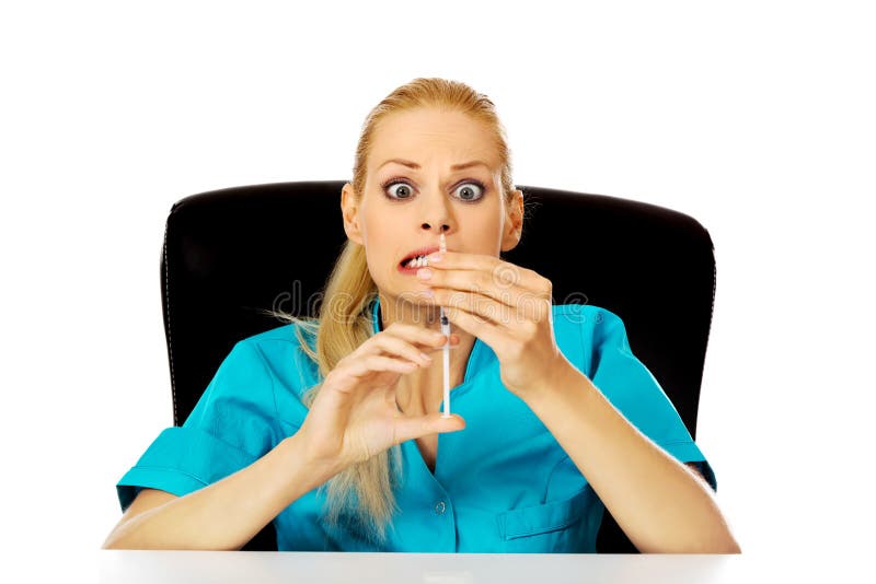 Funny female doctor or nurse sitting behind the desk and holding syringe