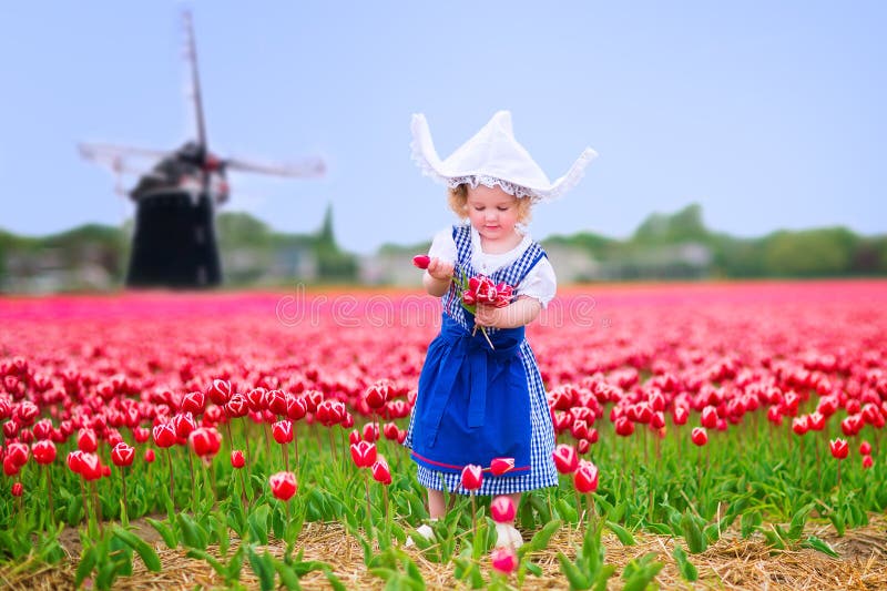 Funny girl in Dutch costume in tulips field with windmill