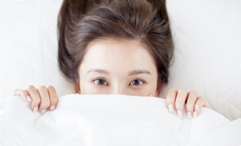 Funny girl lying in bed and hiding under white blanket