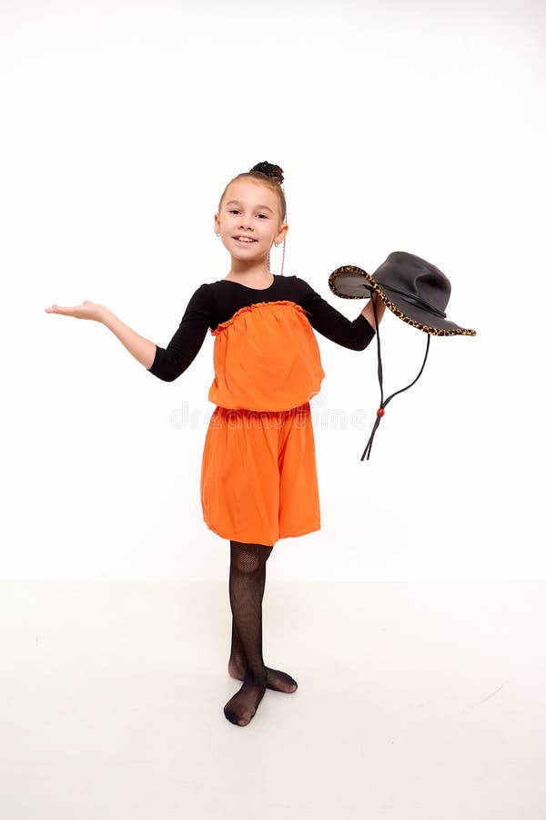 Funny girl in orange dress with hat in the studio with white background during photo shoot. Cute young ballerina inside