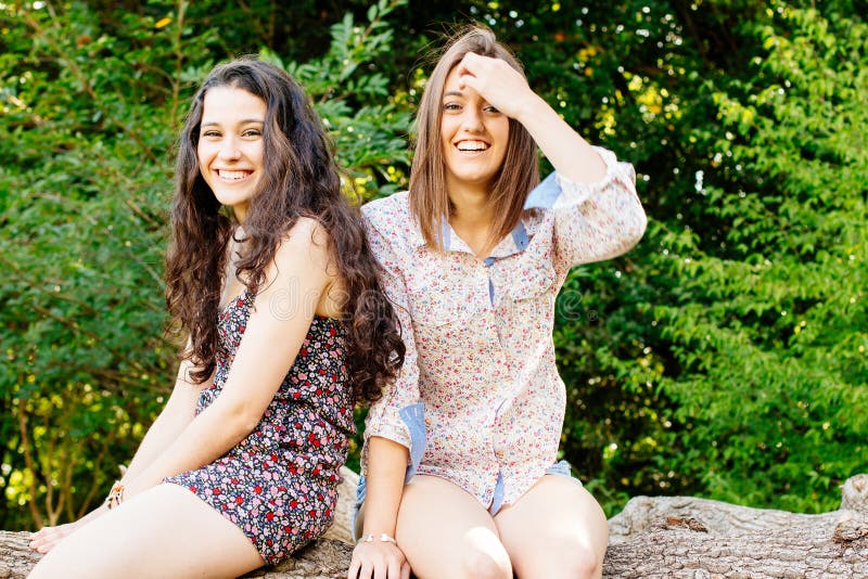 Funny and cute girl friends having fun sitting on a tree trunk. Funny and cute girl friends having fun sitting on a tree trunk