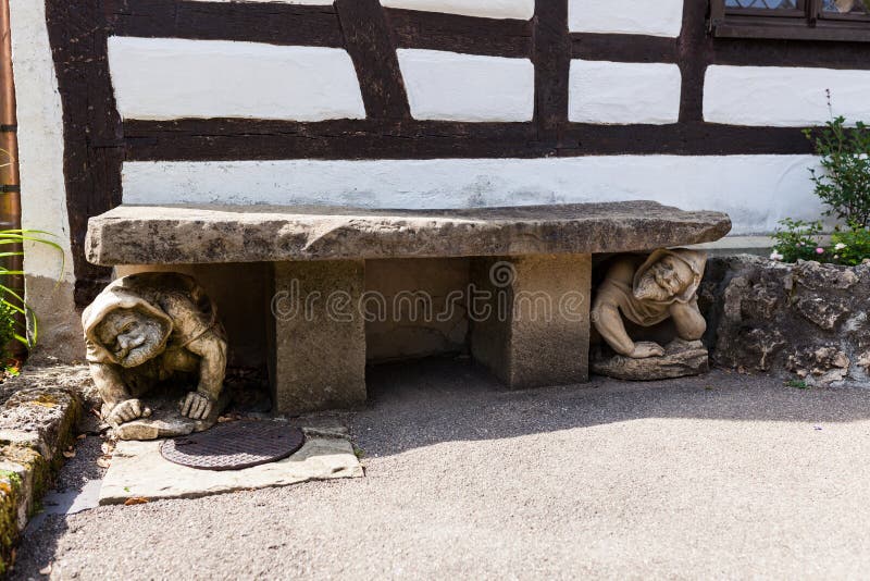 Funny human statue crouching under bench in garden stock images