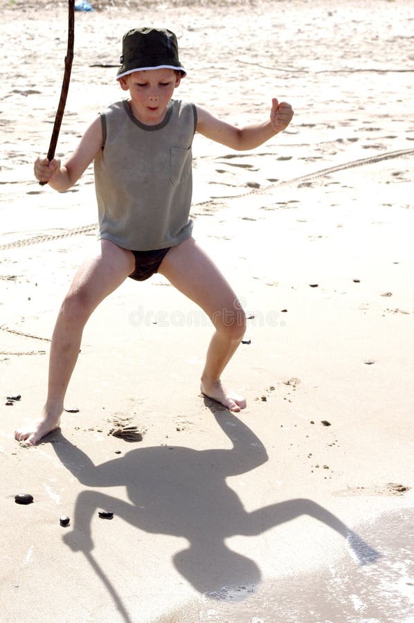 Funny kid playing with stick on a beach sand