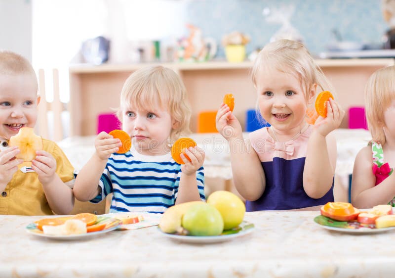 Funny children eating fruits in kindergarten dinning room