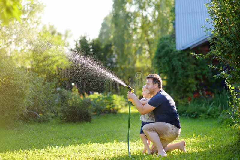 Funny little boy with his father playing with garden hose in sunny backyard. Preschooler child having fun with spray of water