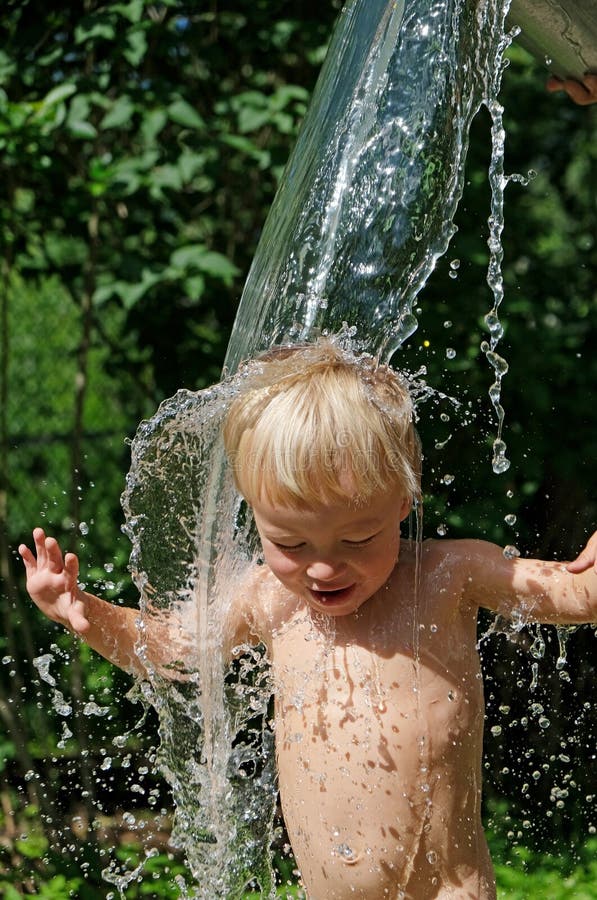 Funny little child  splashing with cold water. Water games on hot day in backyard. Hardening for health. Strengthen your body.