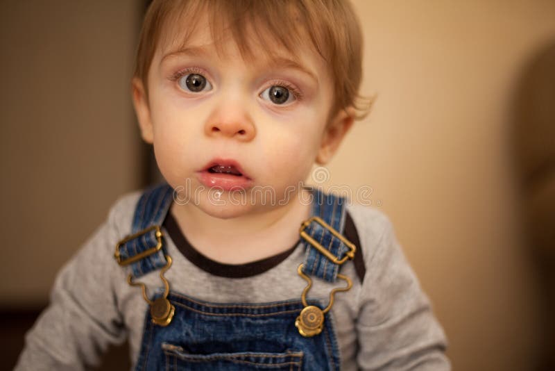 Cute and funny baby boy drooling on his shirt and overalls at home. Cute and funny baby boy drooling on his shirt and overalls at home