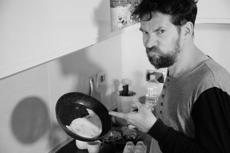 Funny man in kitchen not able to cook an egg unhappy black and white stock image Funny man in kitchen not able to cook an egg unhappy black and white stock image