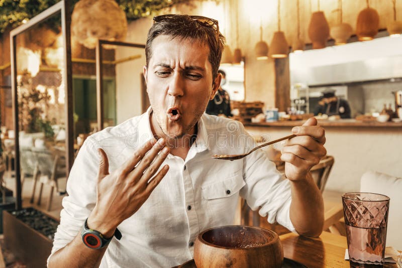 Funny man tries spicy and hot dish from the national cuisine. He`s all red and is trying to cool his mouth with his hand stock photos