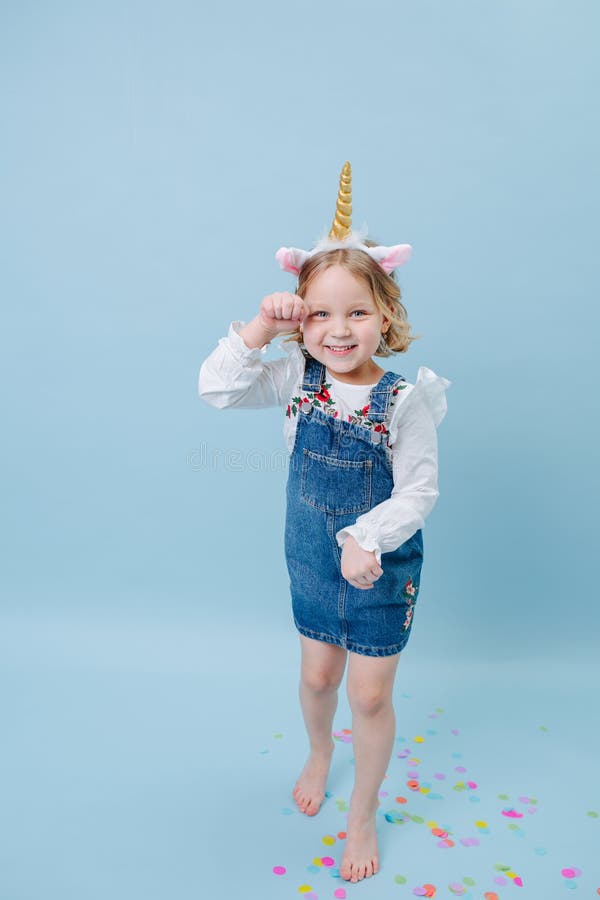 Funny playful little girl in unicorn head band over blue background