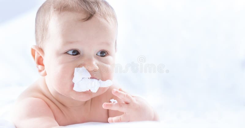 Funny portrait of cute toddler boy lying on bed and trying to eat a paper napkin. Newborn child in bedroom. Baby lies on his tummy stock photo Funny portrait of cute toddler boy lying on bed and trying to eat a paper napkin. Newborn child in bedroom. Baby lies on his tummy stock photo
