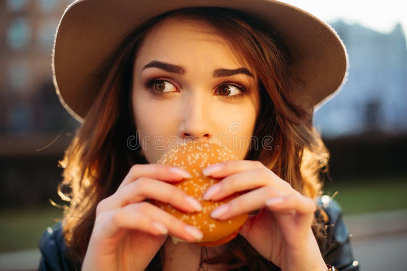 Stylish Brunette Girl In Hat Eating Tasty Hamburger Stock Image