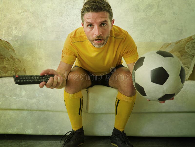 Funny portrait of young stressed and excited football fan man watching soccer game on TV at home couch dressed in team player royalty free stock image Funny portrait of young stressed and excited football fan man watching soccer game on TV at home couch dressed in team player royalty free stock image