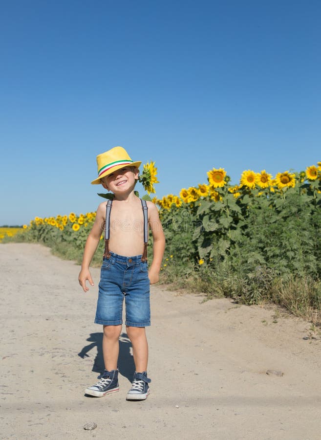 Funny positive boy of 4-5 years old in a yellow hat and shorts on suspenders with one sunflower