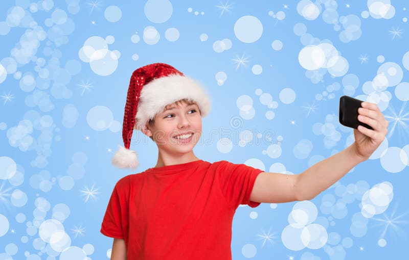 Funny preteen boy in santa hat making selfie on Christmas holiday background.