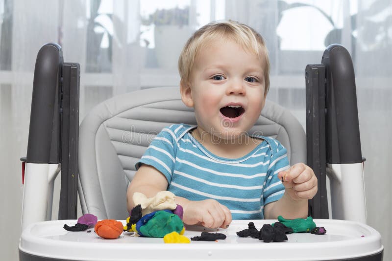 Funny smiling little boy playing with clay dough or Modeling Plasticine, education and daycare concept
