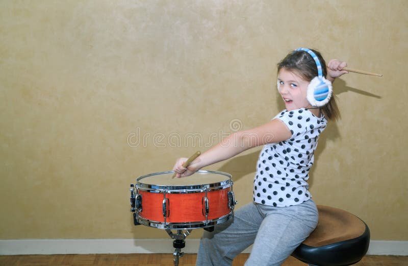 Funny styled little girl in motion practice on snare drum in studio room against vintage wall background