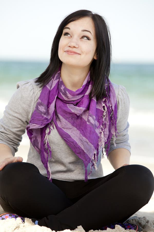 Funny teen girl sitting on the sand at the beach.