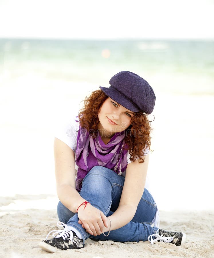 Funny teen girl sitting on the sand at the beach.