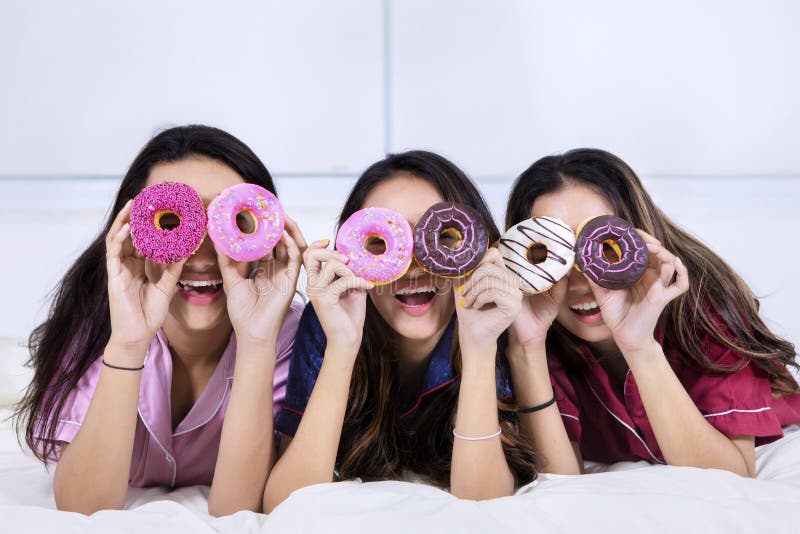 Group of funny teenage girls covering their eyes with donuts on the bed whi...