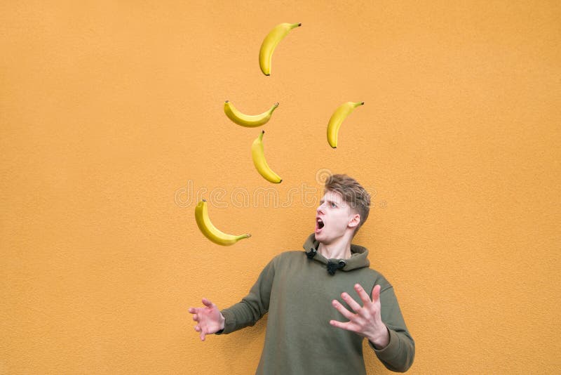 Funny Young Man Juggles with Bananas on the Background of an Orange