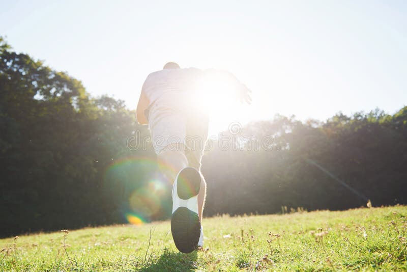 Outdoor cross-country running in summer sunshine concept for exercising, fitness and healthy lifestyle. Close up of feet of a man running in grass. Outdoor cross-country running in summer sunshine concept for exercising, fitness and healthy lifestyle. Close up of feet of a man running in grass.