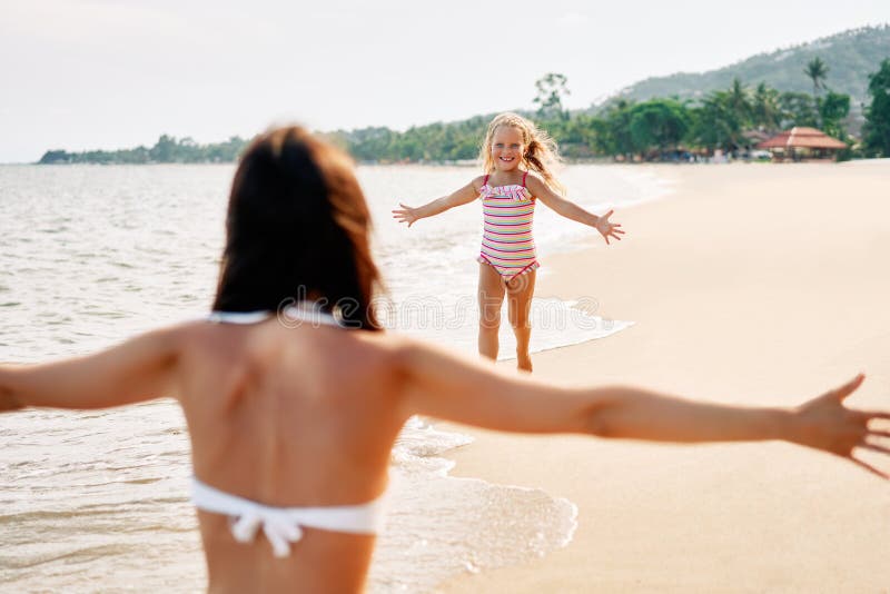 Funzionamento felice della bambina a sua madre per gli abbracci sulla spiaggia tropicale fotografie stock Funzionamento felice della bambina a sua madre per gli abbracci sulla spiaggia tropicale fotografie stock