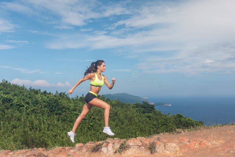 Funzionamento sportivo della traccia della ragazza sul percorso roccioso del giorno soleggiato della montagna immagine stock libera da diritti Funzionamento sportivo della traccia della ragazza sul percorso roccioso del giorno soleggiato della montagna immagine stock libera da diritti