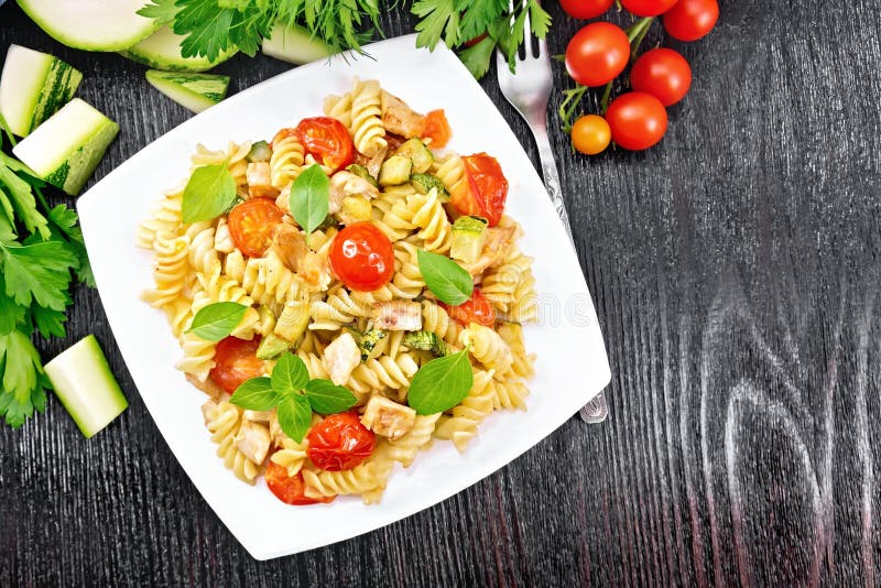 Fusilli with chicken and tomatoes in plate on black board top