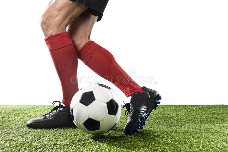 Close up legs and feet of football player in red socks and black shoes running and dribbling with the ball playing on green grass pitch isolated on white background. Close up legs and feet of football player in red socks and black shoes running and dribbling with the ball playing on green grass pitch isolated on white background