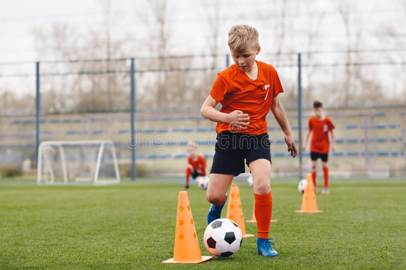 Futbolista masculino en entrenamiento. niño corriendo entre conos durante la práctica en el campo en un día soleado imagen de archivo