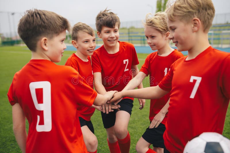 Happy boys play team sport. Kids smiling in school sports team. Junior sports teamwork; kids put hands together. Cheerful children boys players of school soccer team. Happy boys in youth football team. Happy boys play team sport. Kids smiling in school sports team. Junior sports teamwork; kids put hands together. Cheerful children boys players of school soccer team. Happy boys in youth football team