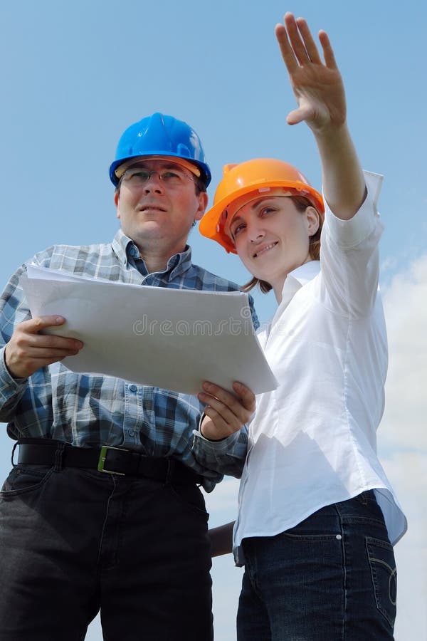 Young couple wearing helmets holding building project documentation visualizing their new future house. Young couple wearing helmets holding building project documentation visualizing their new future house