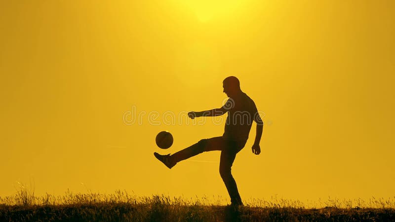 Fußballspieler, der mit dem Ball bei Sonnenuntergang übt