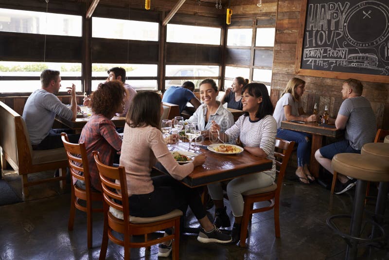 Fyra kvinnliga vänner på lunch i upptagen restaurang, full längd royaltyfri bild