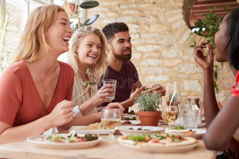 Four young adult friends eating in a restaurant, close up. Four young adult friends eating in a restaurant, close up