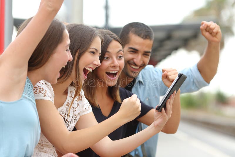 Four euphoric multi ethnic caucasian and arab friends watching tv on a a tablet in a train station. Four euphoric multi ethnic caucasian and arab friends watching tv on a a tablet in a train station