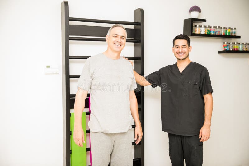 Fysioterapeut And Patient Smiling mot ribbstol i Hospita royaltyfri bild Fysioterapeut And Patient Smiling mot ribbstol i Hospita royaltyfri bild