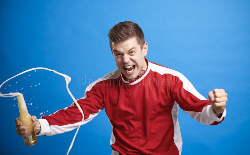 Fã de esportes masculino novo que comemora com uma bebida de derramamento imagem de stock Fã de esportes masculino novo que comemora com uma bebida de derramamento imagem de stock