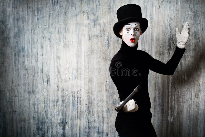 Elegant expressive male mime artist posing with walking stick by a grunge wall. Elegant expressive male mime artist posing with walking stick by a grunge wall.