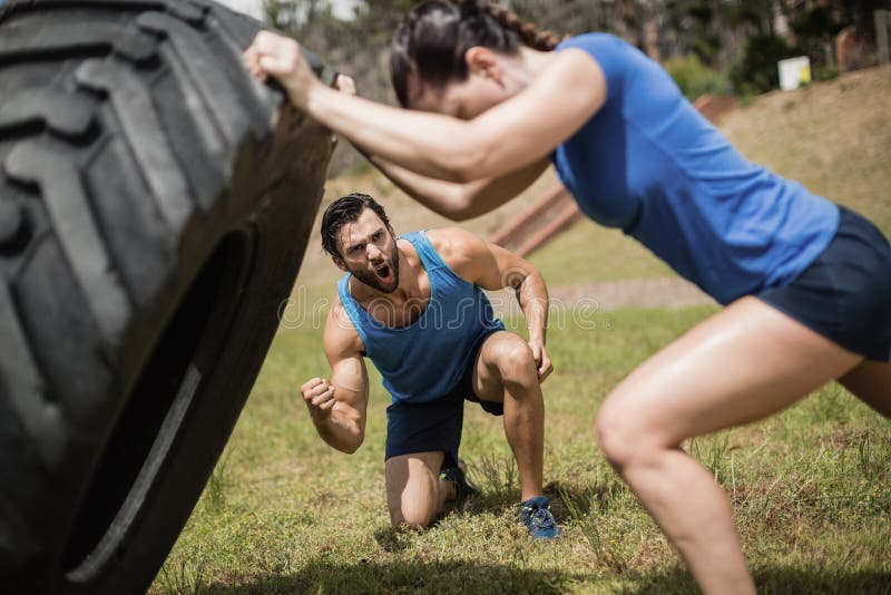 Fit women flipping a tire while trainer cheering during obstacle course in boot camp. Fit women flipping a tire while trainer cheering during obstacle course in boot camp