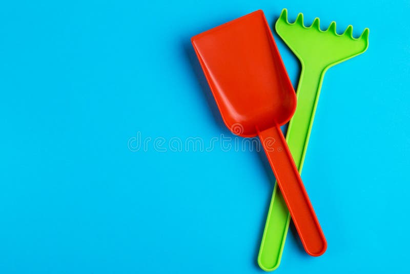 Färgrik leksakspade och att kratta på ljus blå bakgrund arkivbild Färgrik leksakspade och att kratta på ljus blå bakgrund arkivbild