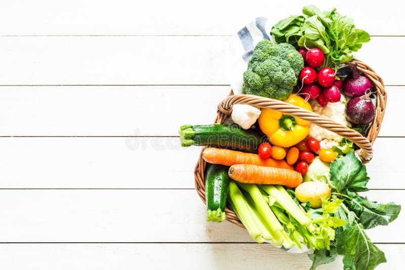 Colorful organic spring vegetables in wicker basket - captured from above top view. White rustic wooden table as background. Layout with free text copy space. Fresh harvest from the garden. Colorful organic spring vegetables in wicker basket - captured from above top view. White rustic wooden table as background. Layout with free text copy space. Fresh harvest from the garden.