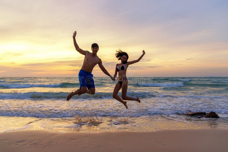 Férias de verão Acople o salto guardando as mãos em tropical no tempo do por do sol da praia em viagens do feriado Povos r dos fe fotos de stock royalty free Férias de verão Acople o salto guardando as mãos em tropical no tempo do por do sol da praia em viagens do feriado Povos r dos fe fotos de stock royalty free