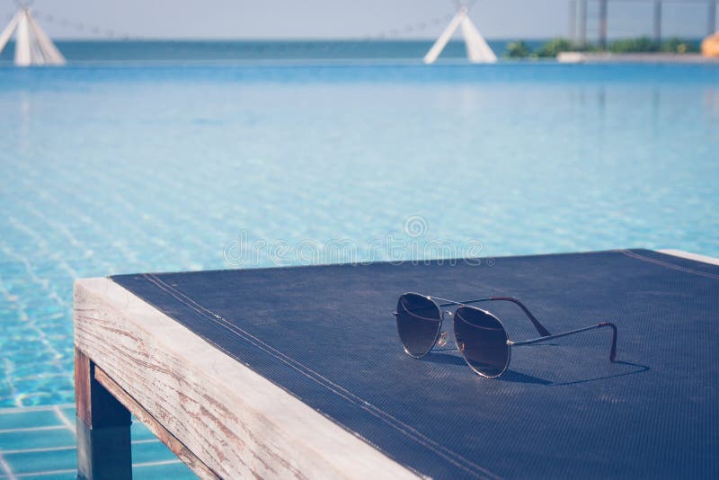 Férias de verão e conceito do feriado: Os óculos de sol puseram sobre o daybed de madeira na piscina com opinião do seascape no f fotos de stock Férias de verão e conceito do feriado: Os óculos de sol puseram sobre o daybed de madeira na piscina com opinião do seascape no f fotos de stock