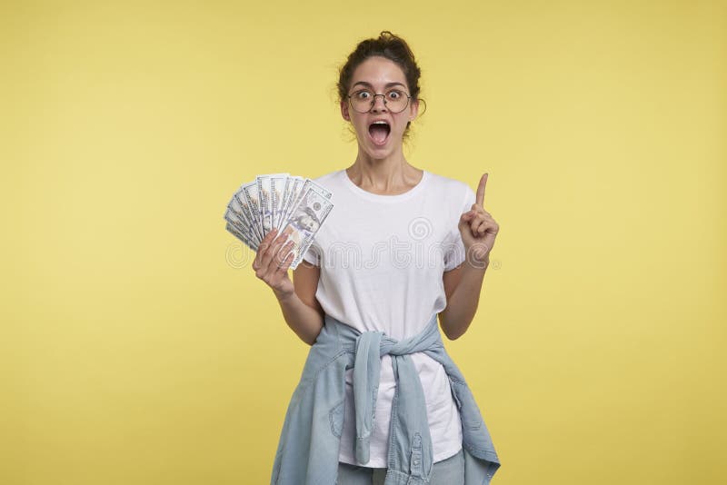 Fêmea feliz e positivamente gritando com uns lotes do dinheiro o a mão, dedo das mostras até o espaço da cópia imagem de stock Fêmea feliz e positivamente gritando com uns lotes do dinheiro o a mão, dedo das mostras até o espaço da cópia imagem de stock