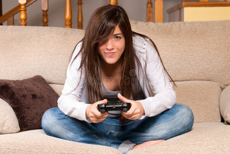 Fêmea nova que joga os videogames que concentram-se no sofá em casa imagens de stock royalty free Fêmea nova que joga os videogames que concentram-se no sofá em casa imagens de stock royalty free