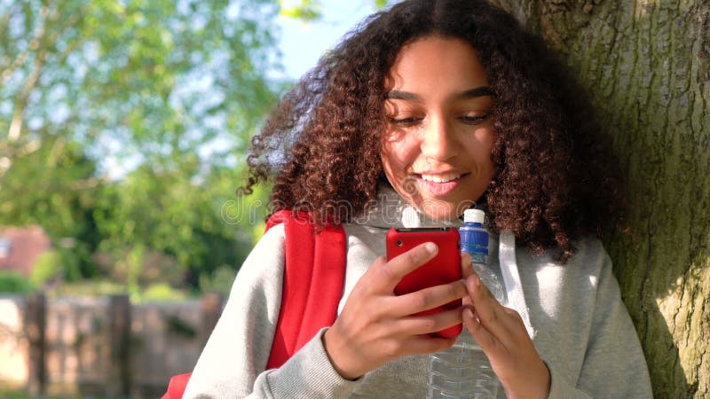 För afrikansk amerikanflicka för blandat lopp benägenhet för tonåring mot ett träd genom att använda mobiltelefonen stock video