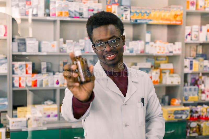 För apotekarevisning för yrkesmässig afrikansk amerikan manlig flaska av medicin enligt recept av kunden i modernt royaltyfri foto För apotekarevisning för yrkesmässig afrikansk amerikan manlig flaska av medicin enligt recept av kunden i modernt royaltyfri foto
