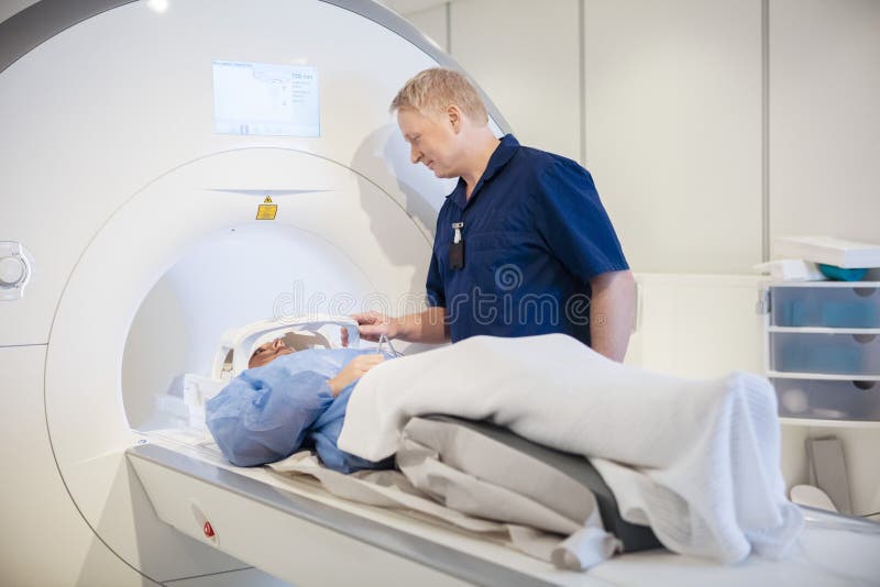 För doktor Putting Coil On tålmodig Head genomgående MRI bildläsning för ` s royaltyfri bild För doktor Putting Coil On tålmodig Head genomgående MRI bildläsning för ` s royaltyfri bild